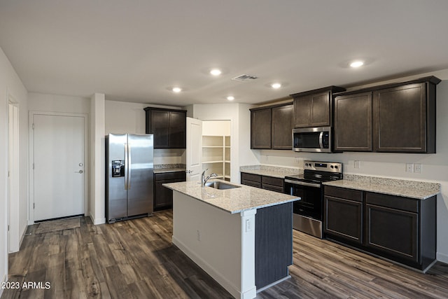 kitchen with light stone counters, dark hardwood / wood-style floors, a center island with sink, stainless steel appliances, and sink