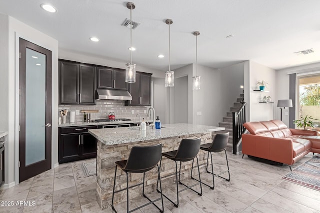 kitchen with a kitchen island with sink, decorative light fixtures, stainless steel gas cooktop, and a kitchen bar