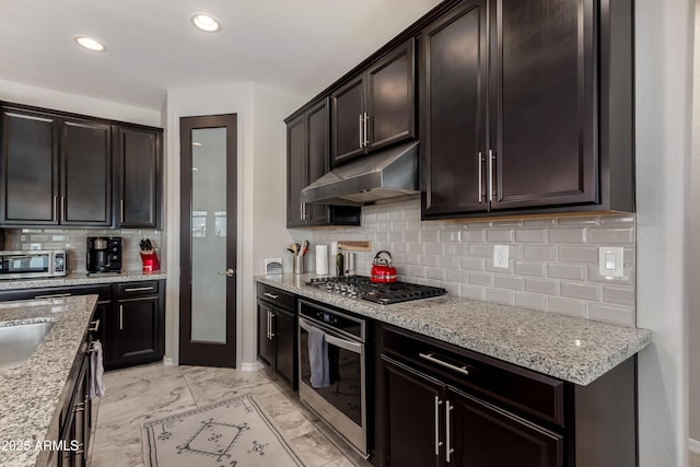 kitchen featuring stainless steel appliances, light stone countertops, dark brown cabinets, and backsplash