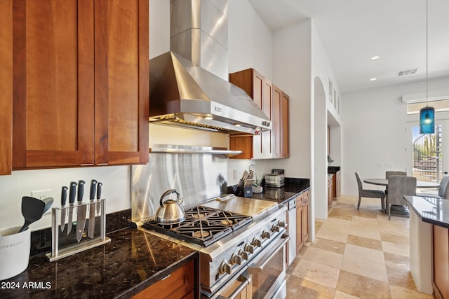 kitchen with decorative light fixtures, high end stainless steel range, dark stone countertops, and wall chimney range hood