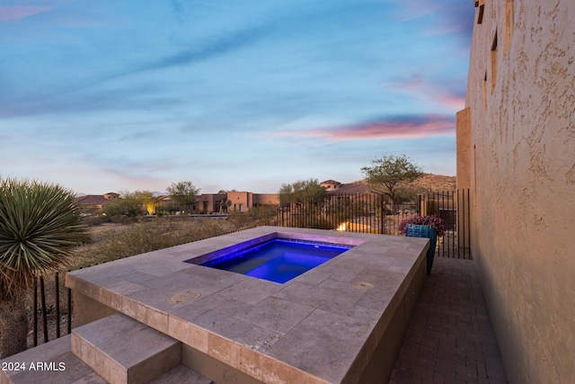 pool at dusk with an in ground hot tub