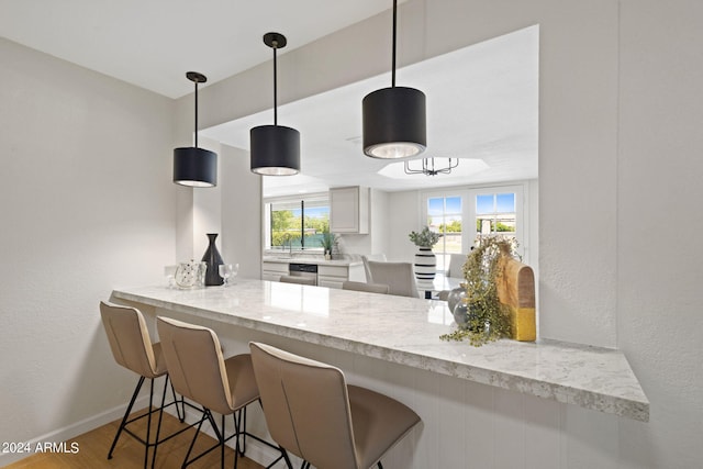 kitchen featuring kitchen peninsula, light stone counters, white cabinets, hardwood / wood-style floors, and hanging light fixtures