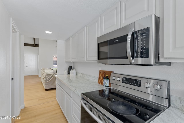 kitchen featuring white cabinets, light stone counters, light wood-type flooring, and appliances with stainless steel finishes