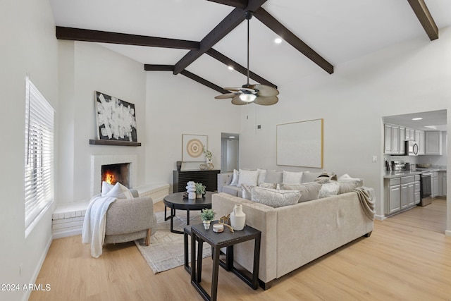 living room featuring ceiling fan, a fireplace, beamed ceiling, and light wood-type flooring