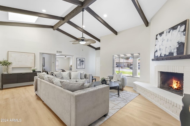 living room with beam ceiling, light wood-type flooring, a brick fireplace, and ceiling fan