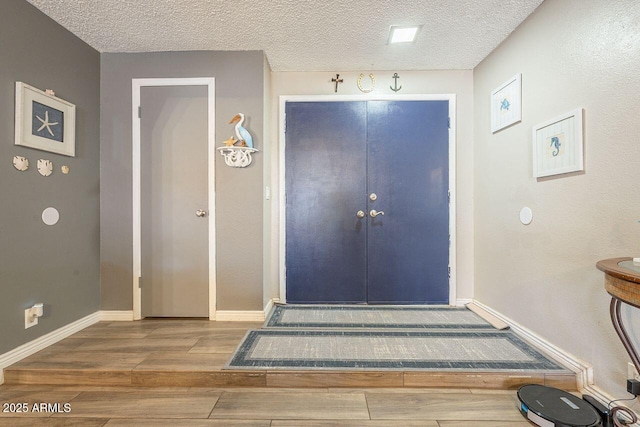 foyer entrance featuring a textured ceiling, baseboards, and wood finished floors