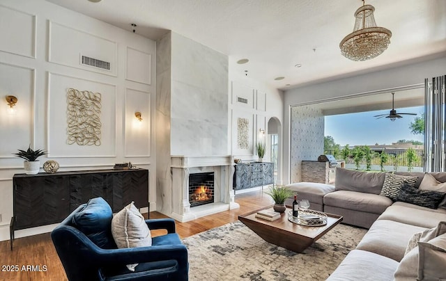 living room with a high end fireplace, wood-type flooring, and ceiling fan