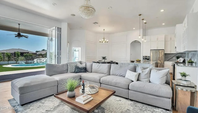 living room featuring ceiling fan with notable chandelier and light wood-type flooring