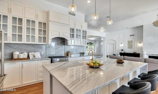 kitchen with sink, a center island with sink, stainless steel range, light stone countertops, and white cabinets