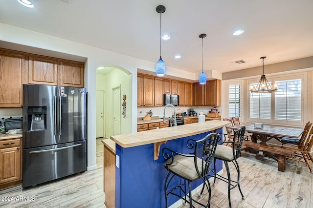 kitchen with a chandelier, decorative light fixtures, a center island with sink, appliances with stainless steel finishes, and light wood-type flooring