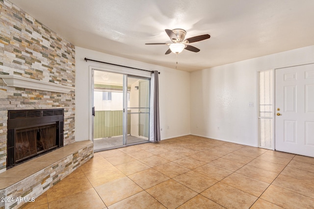 unfurnished living room with light tile patterned flooring, a stone fireplace, and ceiling fan