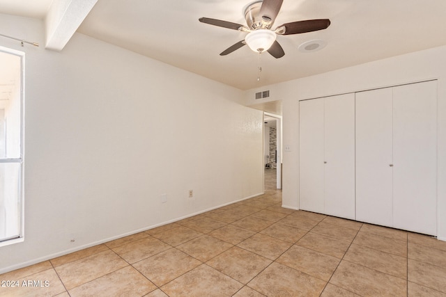 unfurnished bedroom featuring beamed ceiling, light tile patterned floors, a closet, and ceiling fan