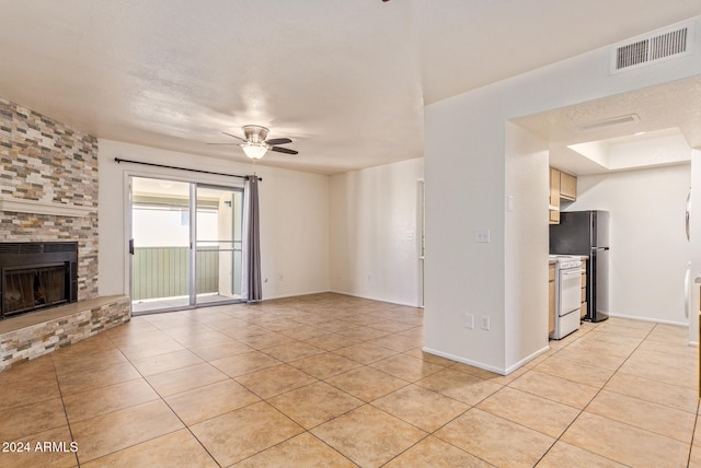 unfurnished living room with ceiling fan, light tile patterned flooring, and a fireplace