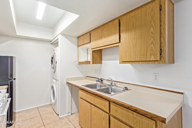 kitchen with sink, stacked washer / dryer, stainless steel refrigerator, and light tile patterned floors