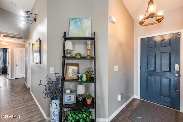 entrance foyer featuring wood finished floors, a notable chandelier, vaulted ceiling, and baseboards