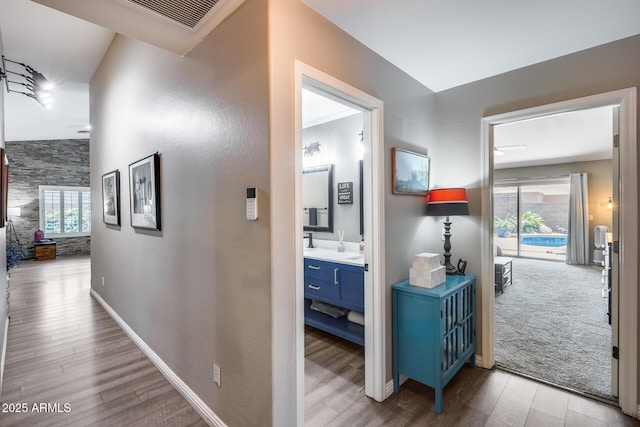 hallway with wood finished floors, baseboards, and visible vents