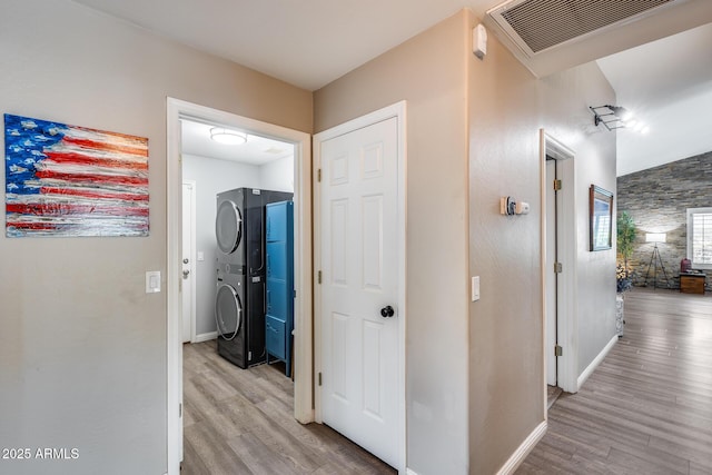 hall with stacked washer / dryer, light wood finished floors, baseboards, and visible vents