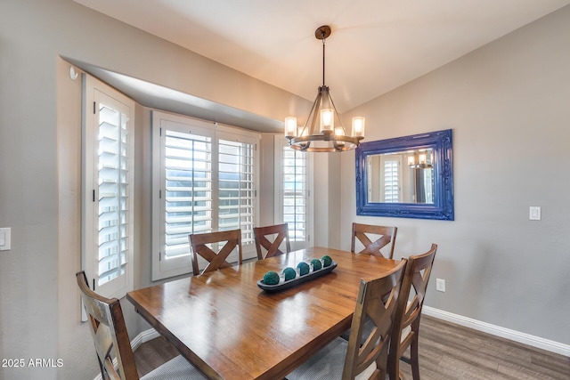 dining space featuring a chandelier, baseboards, vaulted ceiling, and wood finished floors