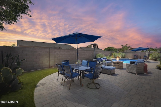 patio terrace at dusk featuring outdoor dining area, a fenced backyard, and a fire pit