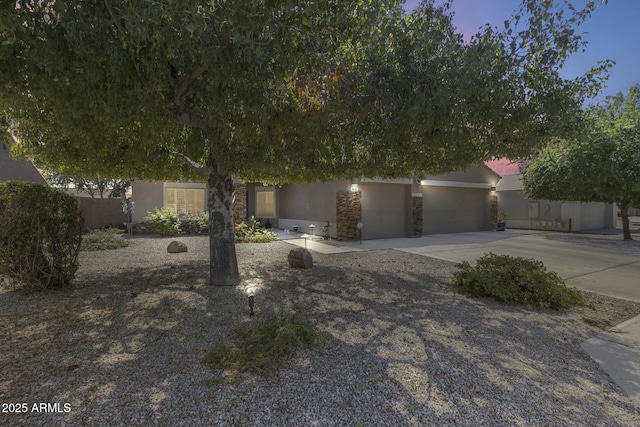 view of property hidden behind natural elements with stone siding, concrete driveway, stucco siding, and fence
