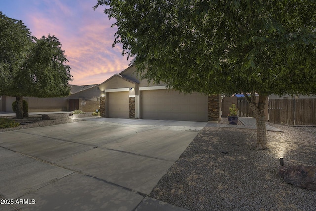 view of property hidden behind natural elements featuring stucco siding, driveway, stone siding, a garage, and fence