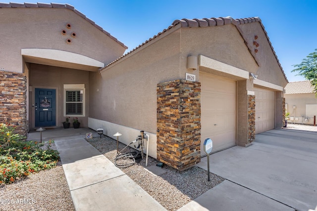 exterior space featuring stucco siding, driveway, stone siding, an attached garage, and a tiled roof
