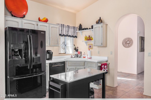 kitchen with a center island, black appliances, sink, light stone countertops, and light tile patterned floors