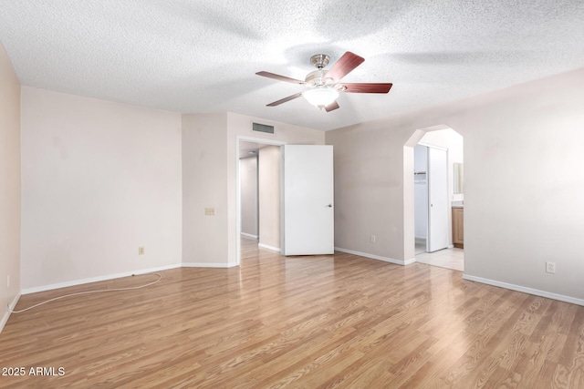 interior space with a textured ceiling, visible vents, baseboards, arched walkways, and light wood-type flooring