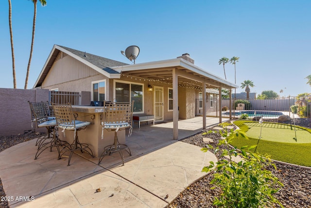 rear view of property with outdoor dry bar, a patio, a fenced in pool, and a fenced backyard