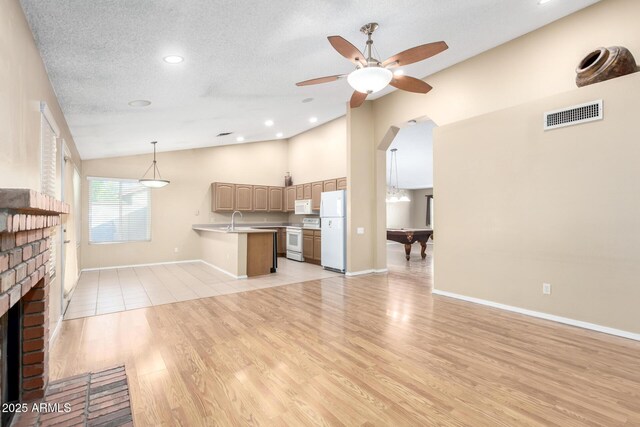 unfurnished living room with lofted ceiling, a sink, visible vents, a brick fireplace, and a ceiling fan