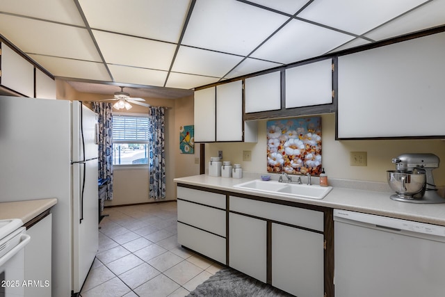 kitchen with a paneled ceiling, sink, white cabinets, light tile patterned floors, and white appliances