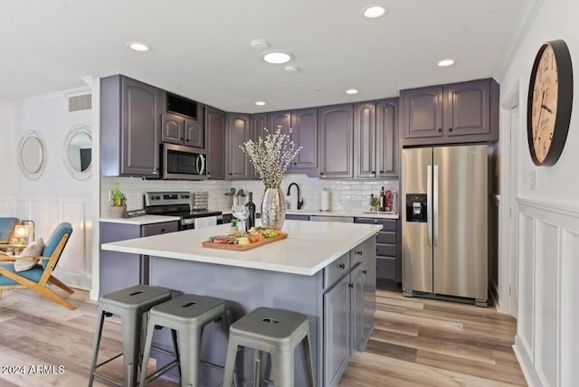 kitchen with a center island, stainless steel appliances, light hardwood / wood-style floors, a breakfast bar, and ornamental molding