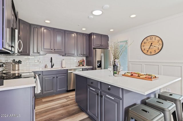 kitchen with a kitchen bar, appliances with stainless steel finishes, sink, a center island, and light hardwood / wood-style floors