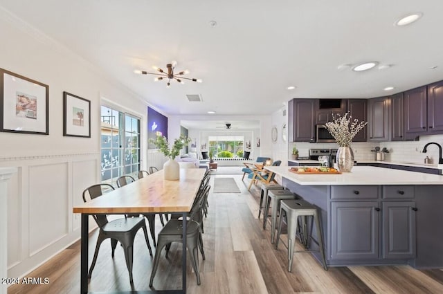 dining area with ceiling fan with notable chandelier, light hardwood / wood-style floors, ornamental molding, and sink