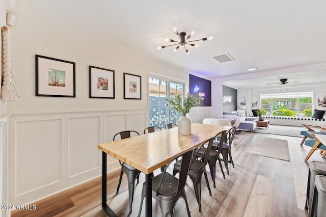 dining room with a wealth of natural light, light hardwood / wood-style floors, ceiling fan with notable chandelier, and ornamental molding