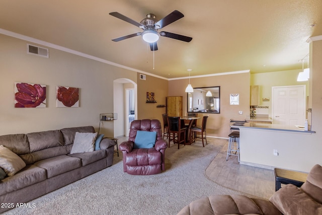 living area featuring carpet floors, visible vents, arched walkways, and ornamental molding