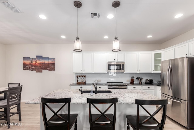 kitchen with stainless steel appliances, a sink, light wood-style floors, a kitchen breakfast bar, and white cabinetry
