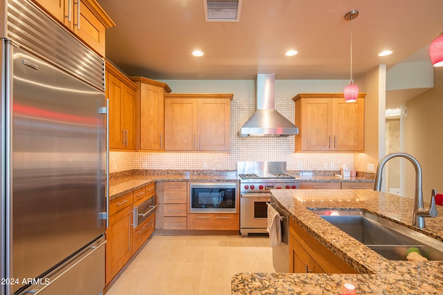 kitchen with built in appliances, sink, hanging light fixtures, wall chimney range hood, and decorative backsplash