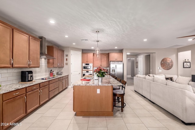 kitchen featuring wall chimney exhaust hood, hanging light fixtures, a breakfast bar, a center island with sink, and appliances with stainless steel finishes