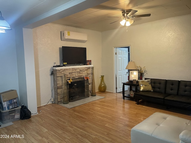 living room featuring a wall mounted air conditioner, wood-type flooring, a stone fireplace, and ceiling fan