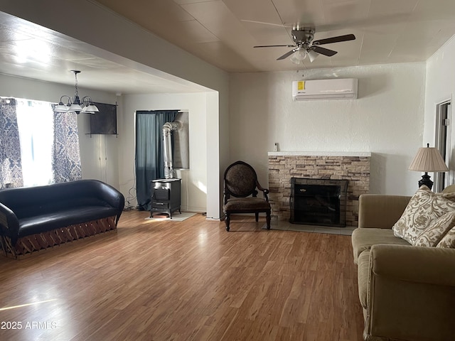 living room with wood-type flooring, ceiling fan with notable chandelier, a stone fireplace, and a wall mounted AC