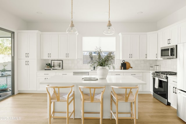 kitchen with decorative light fixtures, a center island, white cabinetry, and appliances with stainless steel finishes