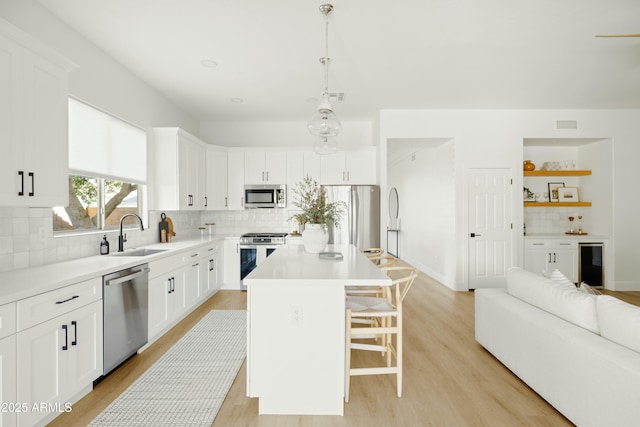 kitchen with white cabinets, decorative light fixtures, a center island, and appliances with stainless steel finishes