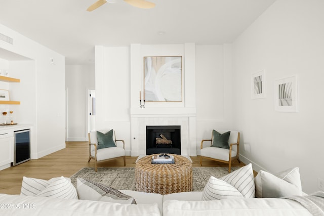 living room featuring indoor bar, a fireplace, light hardwood / wood-style floors, wine cooler, and ceiling fan