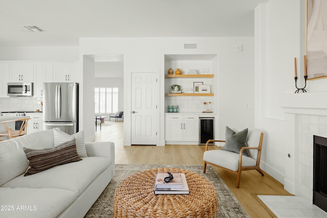 living room with bar area, beverage cooler, a tile fireplace, and light hardwood / wood-style flooring