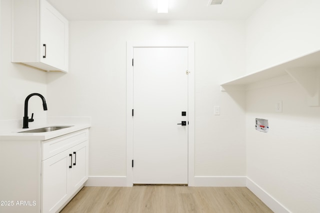 washroom with sink, hookup for a washing machine, light wood-type flooring, and cabinets