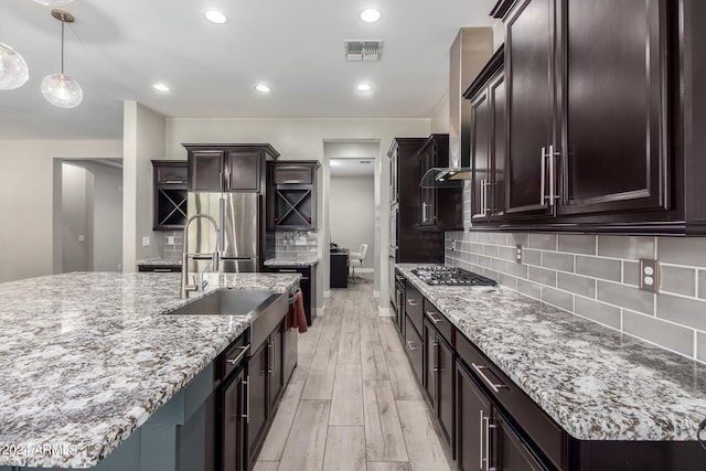 kitchen with appliances with stainless steel finishes, decorative backsplash, light hardwood / wood-style floors, and a kitchen island with sink