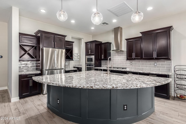 kitchen with wall chimney exhaust hood, appliances with stainless steel finishes, light hardwood / wood-style flooring, and pendant lighting