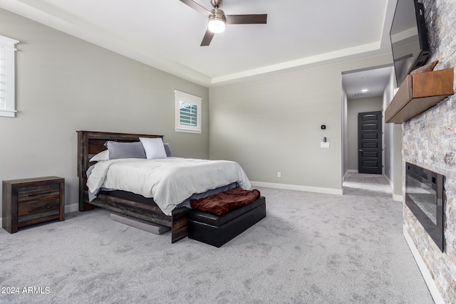 carpeted bedroom featuring ceiling fan and a stone fireplace