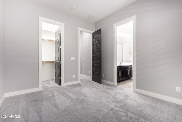 unfurnished bedroom featuring connected bathroom, sink, a closet, a walk in closet, and light colored carpet